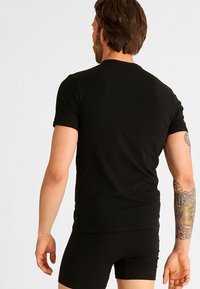 Svart kortermet t-skjorte laget av myk bomull. Fitted design med rund hals og sømløse skuldre. Bakfra har den ingen synlige logoer.