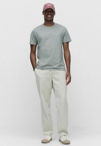 Ljust grå t-shirt med en subtil textur, krämfärgade byxor och en rosa keps. Personen har på sig beige sneakers med vita snören.