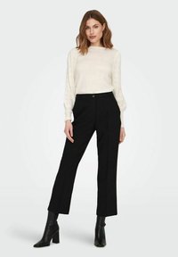 Suéter blanco texturizado con diseño de ojales en las mangas, combinado con pantalones negros de cintura alta y botines negros de tacón.