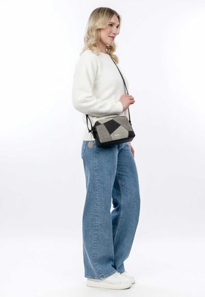 Black and gray patchwork handbag with a rectangular shape, detachable strap, and silver hardware, worn crossbody with casual clothing.