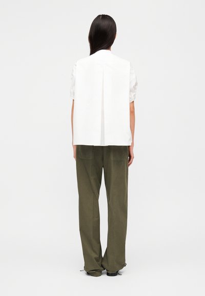 Λευκό αμάνικο τοπ με πλάγιες πιέτες στην πλάτη, συνδυασμένο με φαρδιά παντελόνια σε ελαιώδες πράσινο. Λείος υφασμάτινος υφή, μινιμαλιστικός σχεδιασμός και άνετη εφαρμογή.