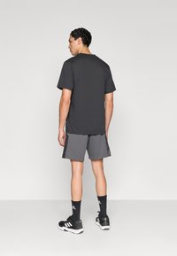 Γκρι βαμβακερό μπλουζάκι, μαύρο και γκρι αθλητικό σορτς, μαύρα παπούτσια με λευκές λεπτομέρειες και μαύρες κάλτσες. Απλός σχεδιασμός, στρογγυλή λαιμόκοψη, άνετη εφαρμογή.