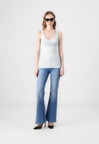 Ljusblå linne med "GUESS"-logga, tillsammans med ljusblå utsvängda jeans och svarta höga klackskor. Modellen bär stora solglasögon.