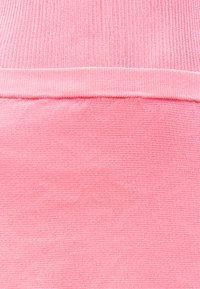 Κοντινή λήψη ροζ υφάσματος που δείχνει δύο διακριτές υφές πλέξης διαχωρισμένες από μια διπλωμένη γραμμή ραφής.