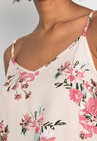 Primo piano di una persona che indossa un top senza maniche floreale di un leggero rosa chiaro, che mette in evidenza la scollatura e l'area delle spalle.