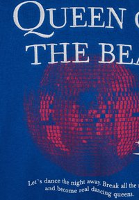 Modra tkanina s grafiko disko krogle v rdeči in roza barvi. Besedilo pravi "Kraljica ritmov" in "Pojdimo plesati do jutra."