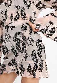 Blommönstrad klänning i ljusrosa med svarta mönster, med långa ärmar, volangdetalj nertill och lätt, genomskinligt tyg.