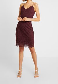 Bordeaux-Farbene Spitzenkleid mit taillierter Silhouette, verstellbaren Spaghetti-Trägern und gewelltem Saum; präsentiert florale Muster und eine glatte Textur.