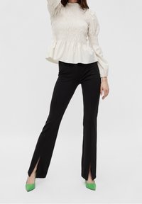 Krämfärgad peplumblus med rynkad textur, svarta tajta byxor med sidokliv och gröna pumps med spetsig tå. Ren, minimalistisk estetik.