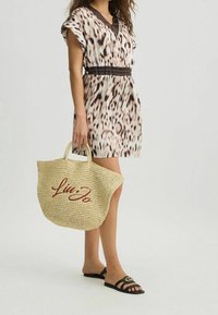 Mekko, jossa on leopardikuvio, lyhyet hihat ja V-kaula-aukko. Beige olkipussit, jossa on punainen "Liu Jo" -logo, yhdistetty mustiin litteisiin sandaaleihin.