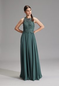 Abito da sera teal con un corpino in pizzo aderente ricamato con cura, scollo alto e una gonna in chiffon plissettata e svolazzante.