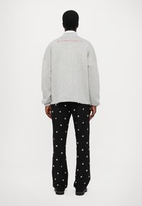 Grijze oversized sweatshirt met rood geborduurde tekst op de achterkant, gecombineerd met zwarte broek met zilveren stippenpatronen.