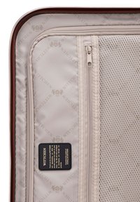 Interieur van een bruine harde koffer met beige voering, met het ingegraveerde merlogo, een mesh ritscompartiment en textiele ritsdetails.