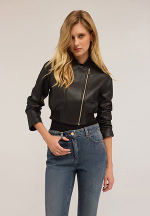 Zwarte leren bomberjack met een ritssluiting aan de voorkant, cropped ontwerp en geribbelde manchetten, gedragen met blauwe denim jeans.