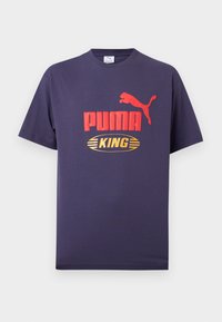 Μπλε ναυτικό T-shirt Puma με κόκκινο λογότυπο Puma και το γράμμα "KING" σε κίτρινο οβάλ, κοντά μανίκια και στρογγυλή λαιμόκοψη.