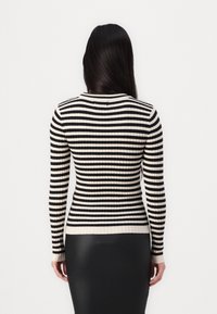 Femme aux longs cheveux noirs portant un pull ajusté à rayures horizontales noires et blanches et une jupe noire, debout de dos.