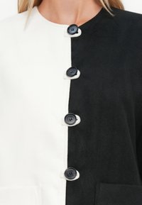 Close-up de um cardigã preto e branco abotoado ao centro, com quatro botões pretos e bolsos em contraste de cada lado.
