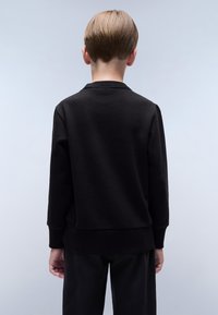 Svart genser med rund hals, ribbestrikkede mansjetter og hem, laget av et mykt materiale. Bakfra viser den et glatt, minimalistisk design.