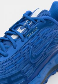 Blue athletic shoe with mesh and synthetic materials, featuring a textured upper, padded collar, and prominent Nike logo. Laces are blue.