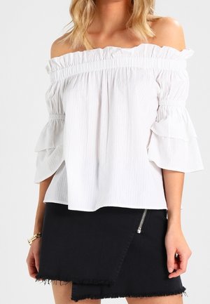 Top bianco senza spalline con scollo arricciato e maniche a campana sovrapposte, abbinato a una gonna di jeans nera con dettaglio in zip argentato.