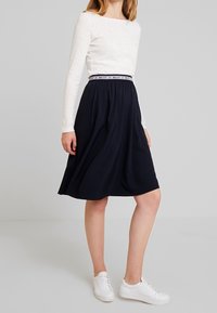 Laivan sininen midi-hame, jossa on ryppyjä, joustava vyötärö ja valkoinen pitkähihainen paita. Yhdistetty valkoisiin lenkkareihin rentoa ilmettä varten.