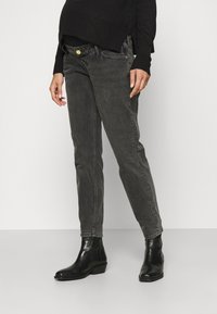 Harmaat farkut, joissa on kapea fit, kultanappi ja etutaskut, yhdistetty mustiin nilkkabootseihin ja löysään mustaan toppiin.