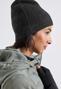 Charcoal knitted beanie with ribbed edge, worn with a light green puffer jacket. Hand covered by a black ribbed knit glove.