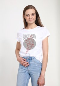 Hvid bomulds t-shirt med et grafisk billede af en figur med et våben, omridset i rødt, med teksten "BLACK WIDOW" ovenfor i grå.