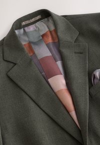 Blazer vert foncé avec larges revers et doublure en soie patchwork multicolore visible à l'intérieur du col et de l'ouverture avant.
