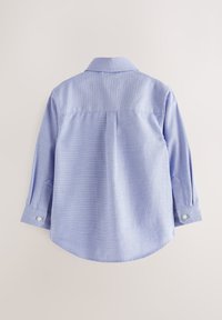 Chemise bleu clair à manches longues avec poignets boutonnés, vue de dos sur un fond clair uni.