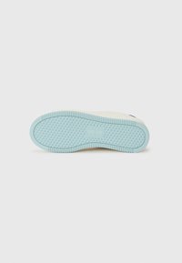 Sneaker dengan sol karet berwarna biru muda yang memiliki tekstur, dilengkapi dengan pola untuk pegangan. Bagian atas terbuat dari kain berwarna krem dengan aksen minimal.