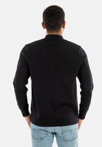 Maglione a collo alto di colore blu navy, realizzato a maglia, con maniche lunghe e vestibilità aderente, rifinito con polsini a coste. La vista posteriore mette in risalto la semplicità e la texture.