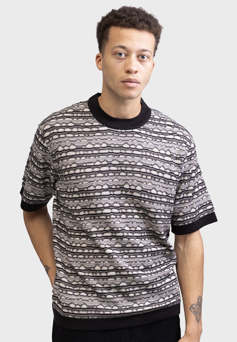 Short-sleeve sweater in black and white with a textured pattern of horizontal lines. Features a ribbed black collar and cuffs.