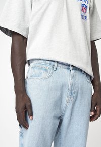 Harmaa ylisuuri t-paita sinisellä graafisella printillä ja lyhyillä hihoilla, yhdistettynä vaaleansinisiin farkkulegginsseihin, joissa on klassinen 5-taskurunko.