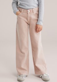 Heledad roosad laia lõikega teksad, valmistatud denimist, millel on ees nööpkinnitused, vööaasad ja küljetaskud. Kandmiseks sobitatud halli pika varrukaga särk ja tossud.