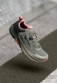 Scarpa da corsa con una tomaia in mesh grigia e dettagli rosa, presenta una suola testurizzata e un'imbottitura spessa, progettata per stabilità e trazione.