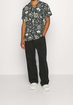 Chemise noire à manches courtes avec des motifs blancs abstraits, assortie à un pantalon noir et des baskets blanches. Tissu en coton, coupe décontractée.