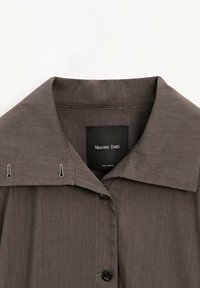 Camicia grigia con bottoni, dal colletto classico, realizzata in un tessuto testurizzato, con etichetta nera e dettagli di cucitura a contrasto.
