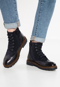 Námorně modré kotníkové boty s kombinací semiše a lakované kůže, s brogue designem, šněrováním, bočním zipem a pevnou gumovou podrážkou.