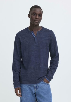 Navy lange mouwen henley-shirt van textuurstof, met een drieknoopssluiting en contrasterende blauwe halslijn en manchetten. G gedragen met licht denim jeans.