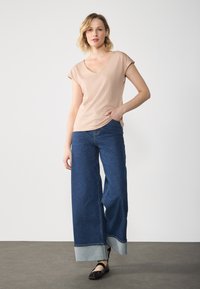 Lys beige V-hals top med korte ærmer parret med knælange, brede blå denimbukser med en kontrasterende opsmøg og sorte flade sko.