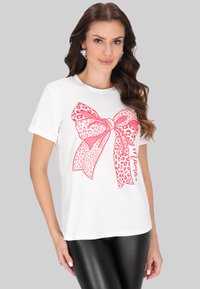 Hvid t-shirt med en stor grafisk lyserød leopardprint-sløjfe på forsiden. Rund hals, korte ærmer og afslappet pasform.