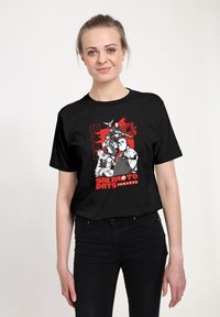 Usměvavá žena v černém tričku s červenými a bílými anime postavami a japonským textem z manga série "Sakamoto Days".