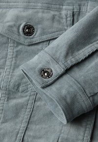 Jasnoniebieska tkanina kordowa z teksturowym wzorem, z wyraźnym czarnym napem i starannym przeszyciem na mankiecie.