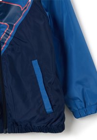 Blauer Windbreaker mit marineblauen und blauen Paneelen, Reißverschluss vorne, elastischen Bündchen und zwei Seitentaschen. Glattes, leichtes Material.