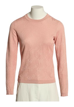 Pull rose à manches longues et col rond avec un motif subtil en relief, porté sur un buste de mannequin avec un pantalon blanc.