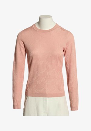 Pull rose à manches longues et col rond avec un motif subtil en relief, porté sur un buste de mannequin avec un pantalon blanc.