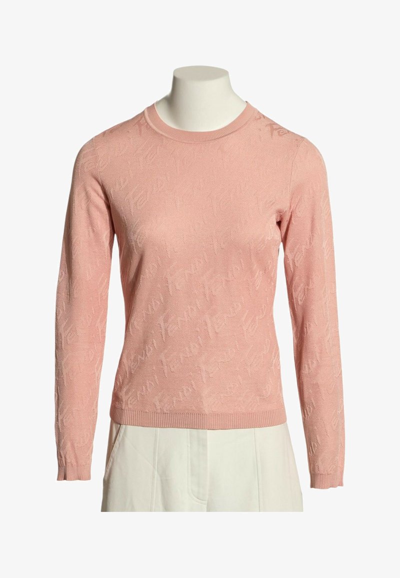 Pull rose à manches longues et col rond avec un motif subtil en relief, porté sur un buste de mannequin avec un pantalon blanc.
