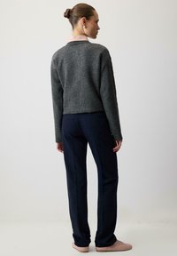 Pulover gri tricotat cu un design scurt, tiv ondulat și mâneci lungi, combinat cu pantaloni bleumarin și adidași de culoare piersici.