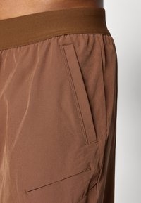 Brune shorts med en myk, elastisk midje, med lommer på siden og en glatt tekstur. Stoffet ser lett og holdbart ut.